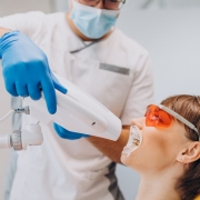 A dentist wearing gloves and a mask uses a whitening device on a patient with protective glasses and a mouthguard in a dental clinic.