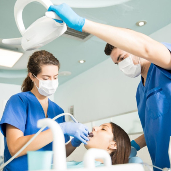 A woman sits in a dental chair while a dentist checks her teeth.